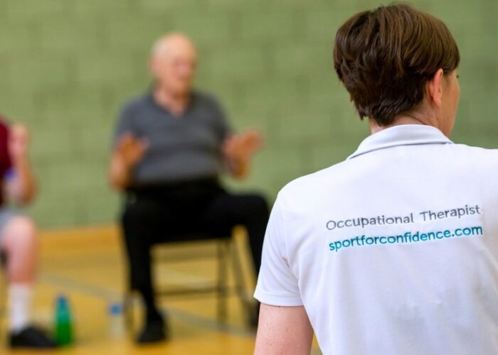 Occupational therapist leading an inclusive seated exercise session in a sports hall