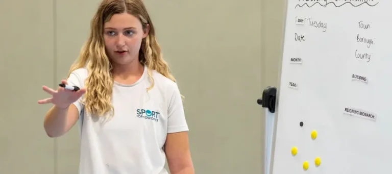Standing woman talking with outstretched arm next to a white board