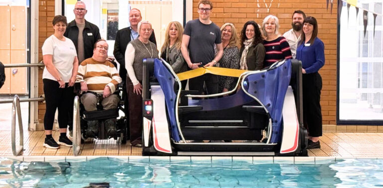 Group gathered beside a swimming pool to celebrate the installation of an accessible pool pod lift