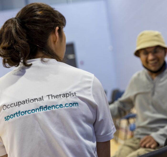SFC Careers Occupational therapist in a white branded shirt speaking with a smiling seated client in a rehabilitation or therapy setting.