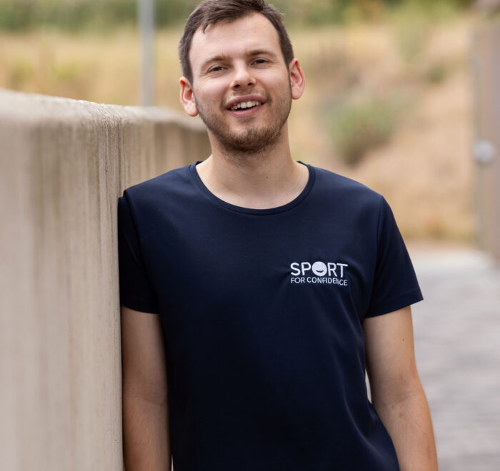Volunteer A Sport for Confidence volunteer leaning against a wall smiling at the camera