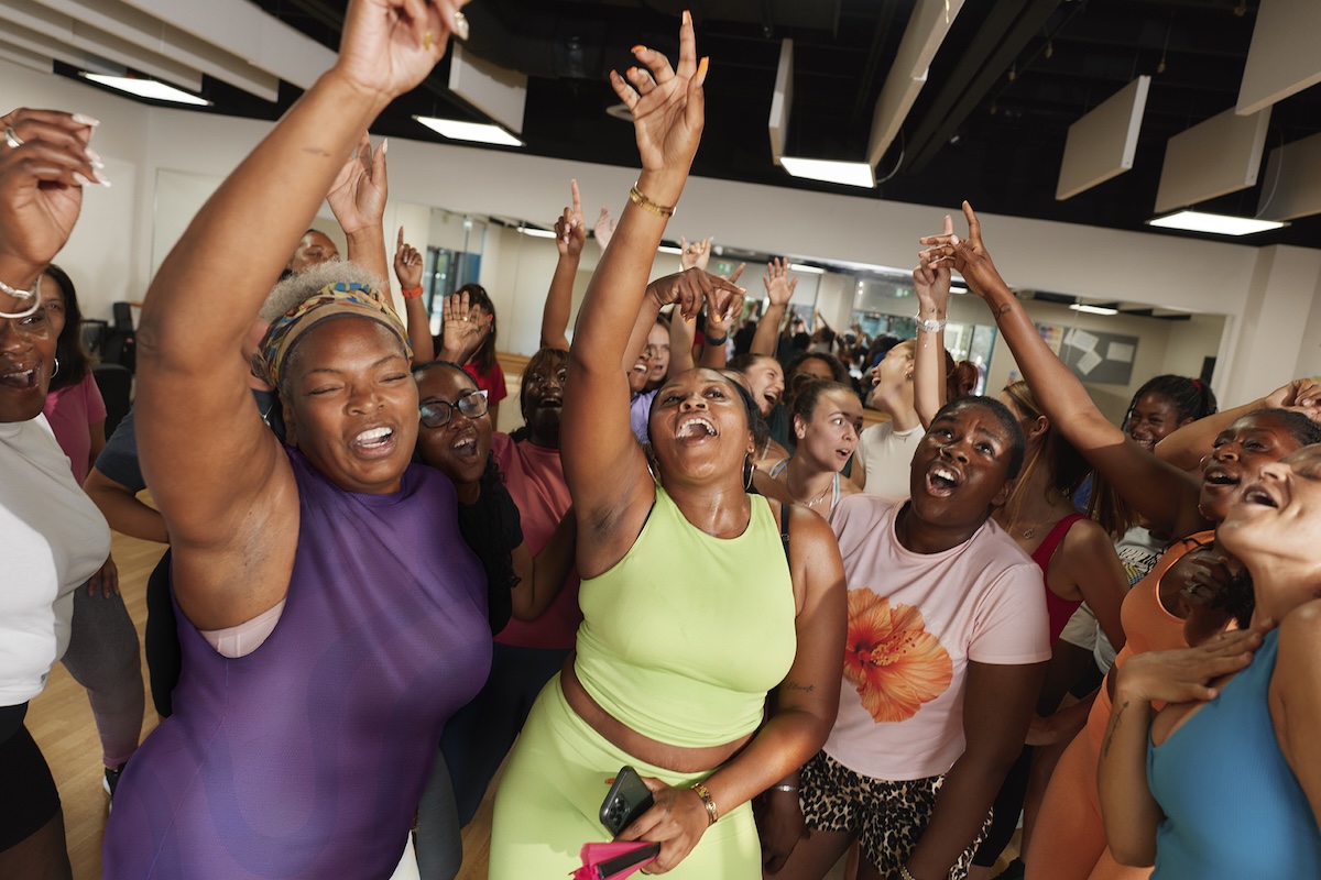 Energetic fitness class participants cheer together in a bright studio, raising hands, smiling, celebrating community, movement, and empowerment today, togetherness.