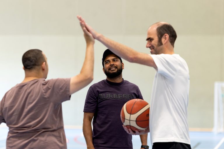 A Sport for Confidence occupational therapist high fiving a participant while another participant looks on, holding a basketball.