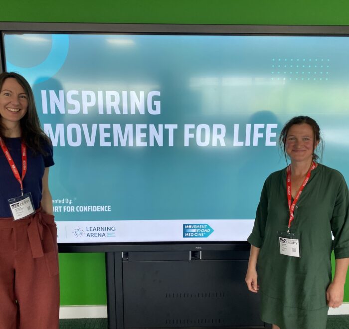 IMG_2662 Two attendees stand beside a screen displaying “Inspiring Movement for Life” during a movement and wellbeing training session.