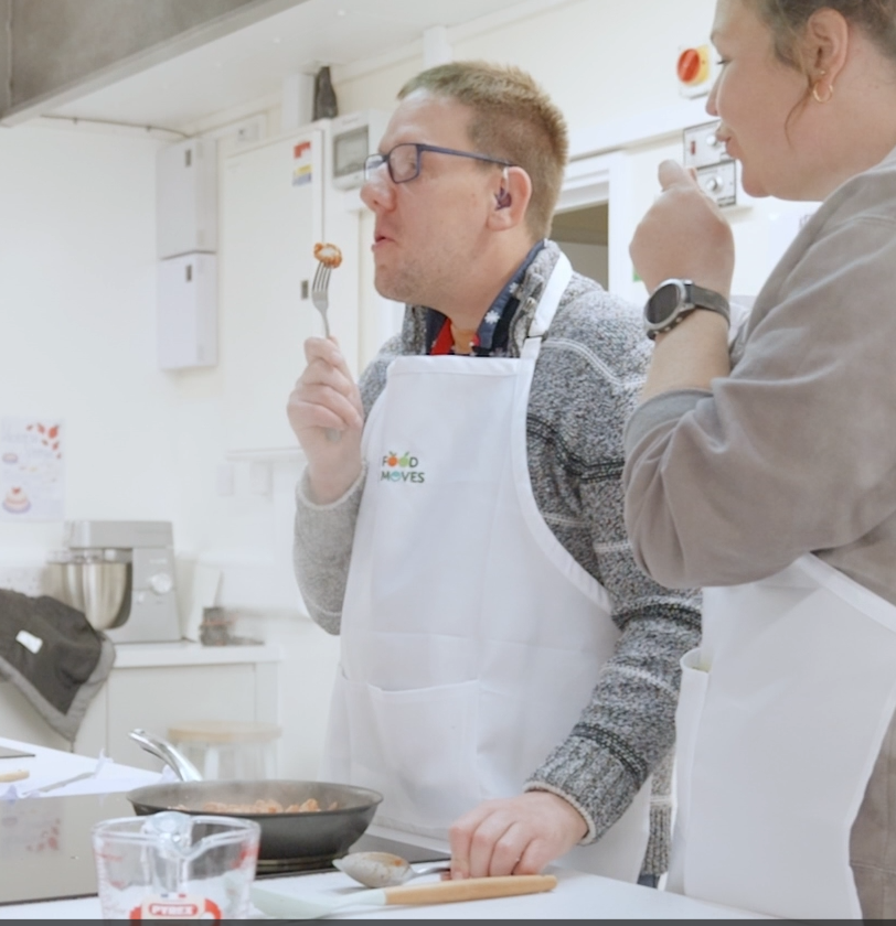 Participant wearing a cooking apron tasting food during a group cooking activity in a community kitchen.