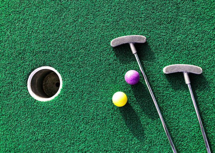 iStock-1445593235 Golf clubs and balls laid next to a hole on a putting green