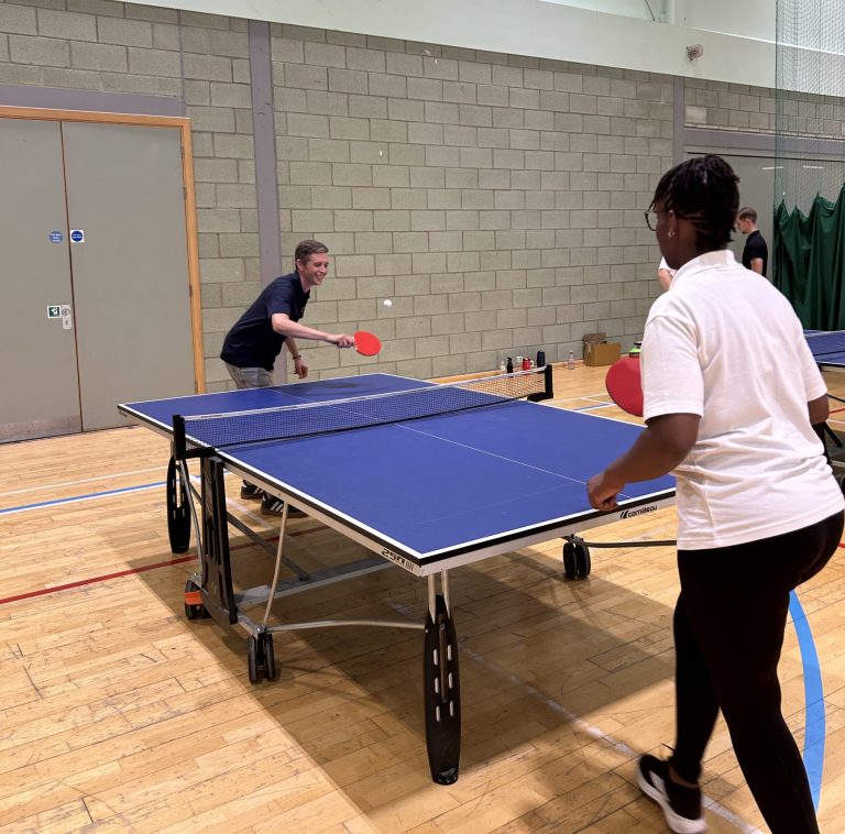 Two people playing table tennis in a leisure centre sports hall.
